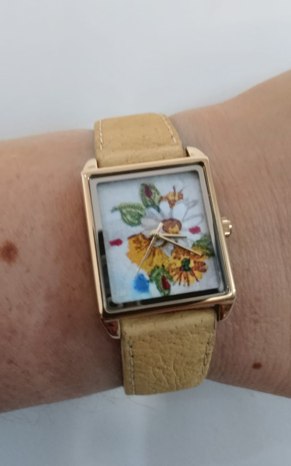 PP Atelier Floral no pulso, com gravura de flores no mostrador, caixa retangular dourada e pulseira bege.